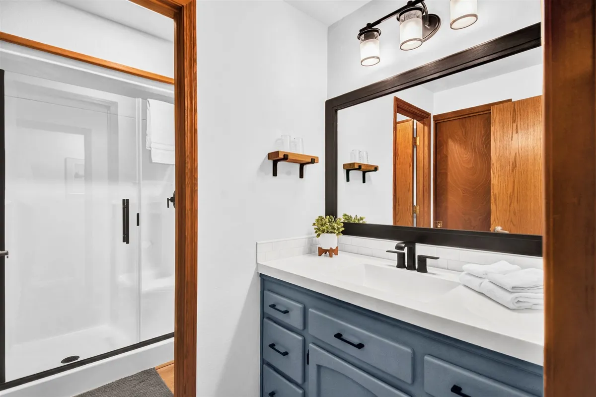 A modern and inviting bathroom featuring a blue vanity, large mirror, and glass-enclosed shower, exuding a sense of freshness and tranquility ideal for morning routines or relaxing after a long day.