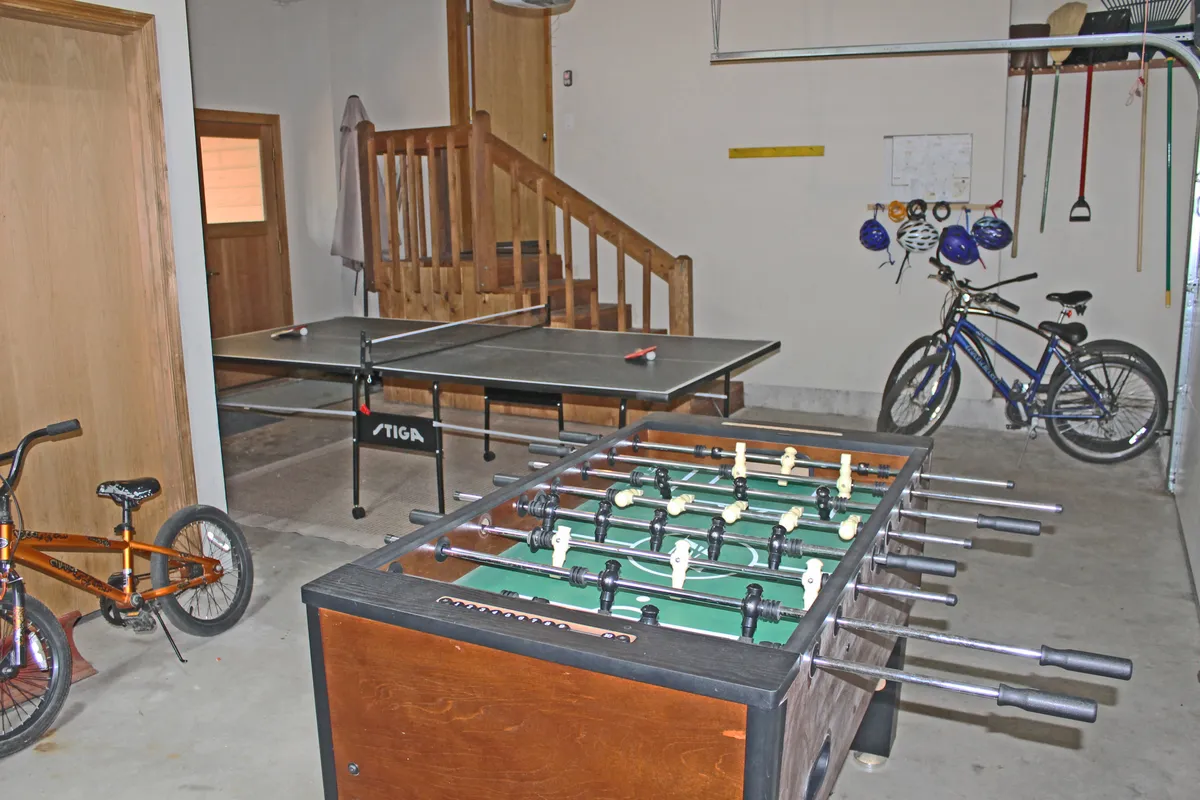 A fun, energetic garage scene featuring both a foosball and ping pong table alongside bicycles and a staircase, capturing the playful spirit of the space and suggesting additional recreation options, like biking.