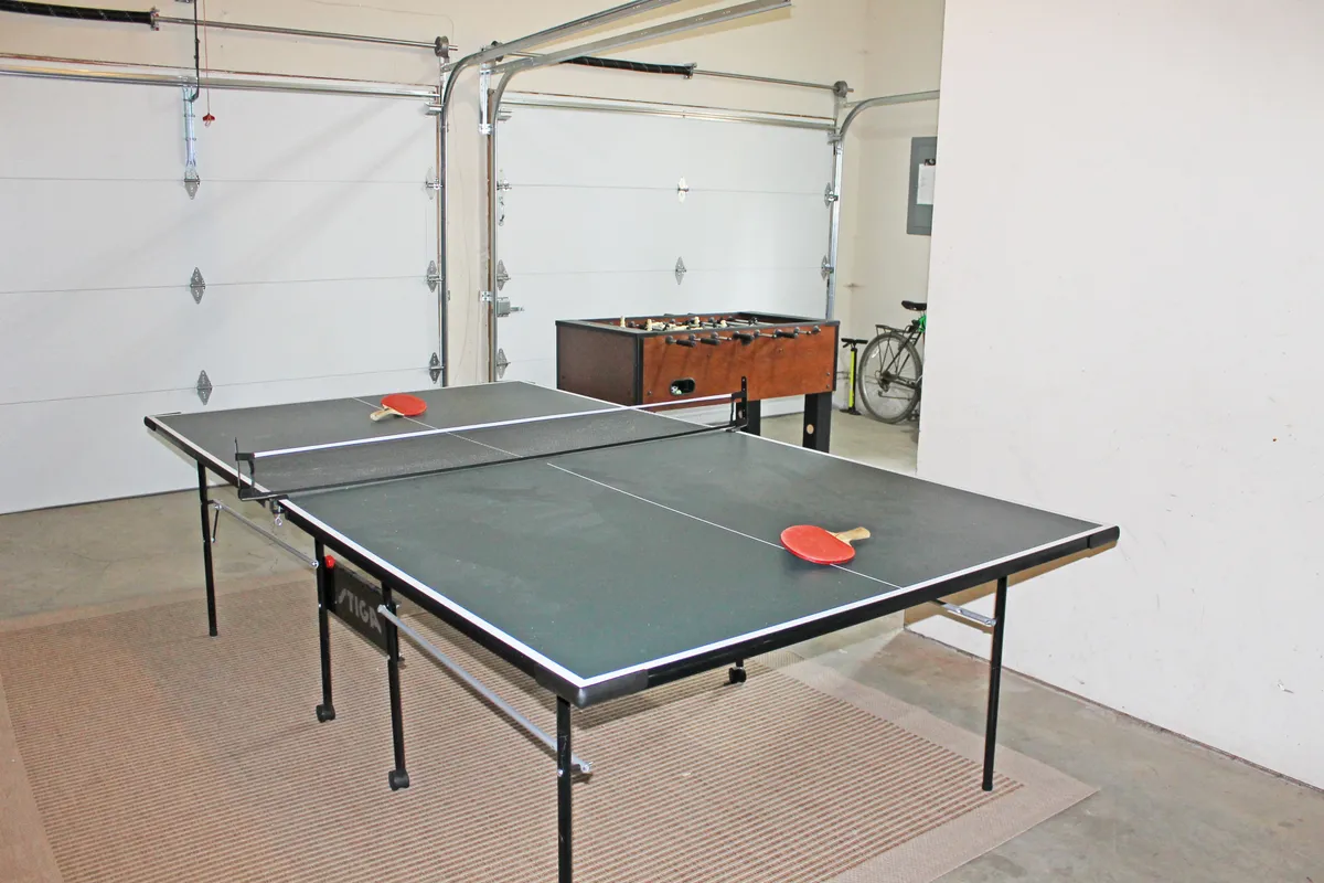 This image showcases the garage game area, complete with both a ping pong table and a foosball table, as well as visible garage doors. The space looks playful and relaxed, inviting groups to engage in friendly competitions or game nights.