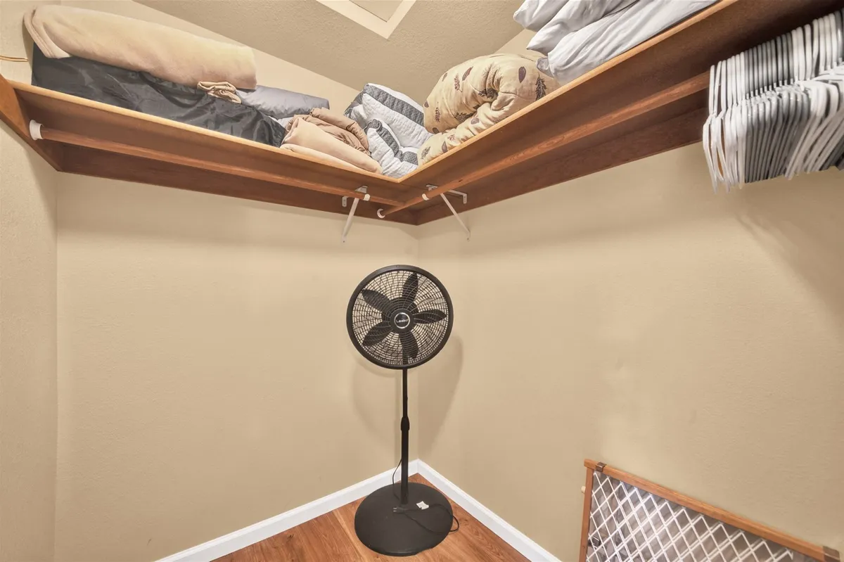 A practical storage area with shelves stacked with folded linens, a standing fan, and clothes hangers—ideal for organizing clothing and gear after active days outside.