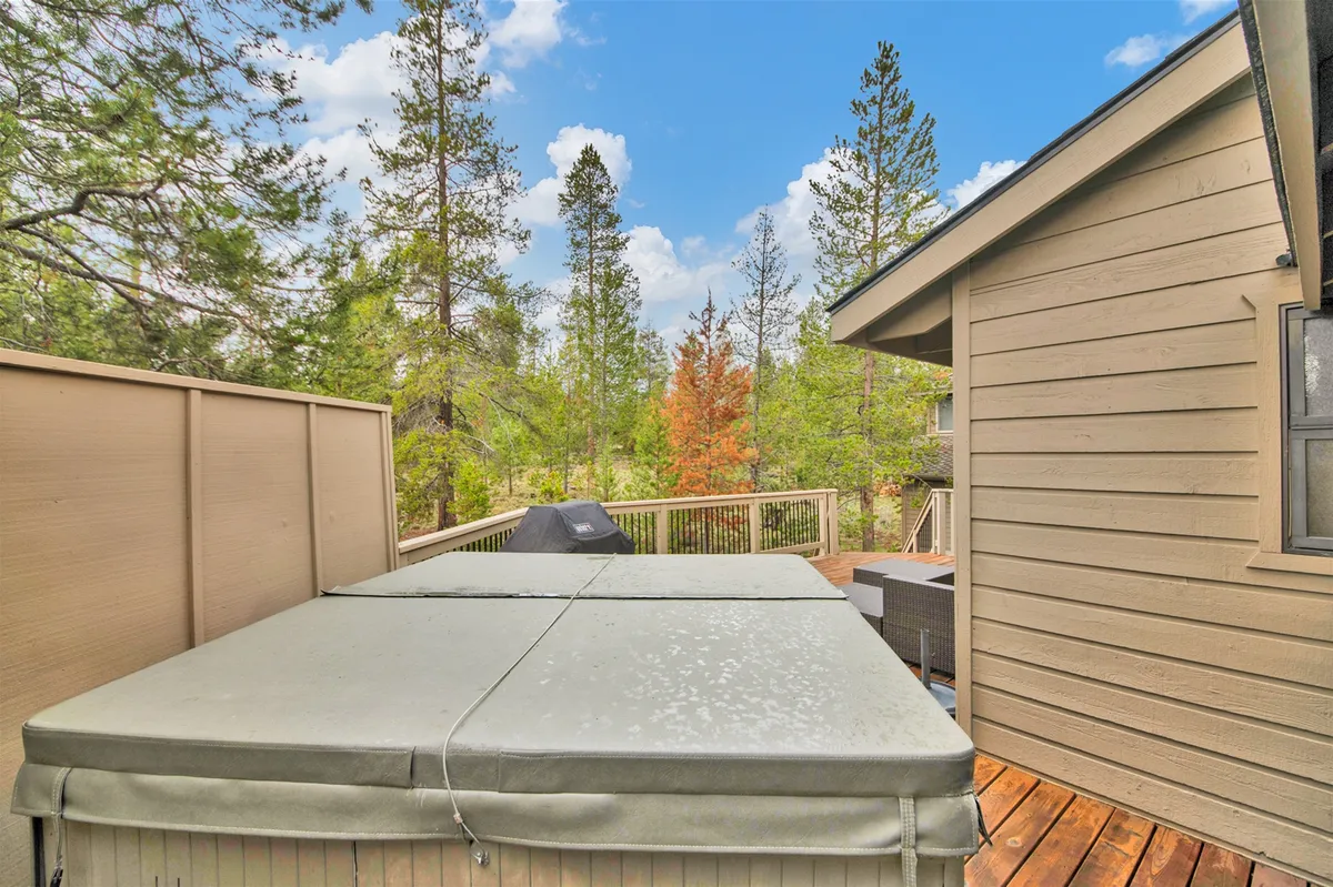 A serene, elevated deck with a bubbling hot tub set among tall trees, creating an oasis for relaxation. The deck offers views of the natural surroundings, enhancing the sense of seclusion and immersion in nature.