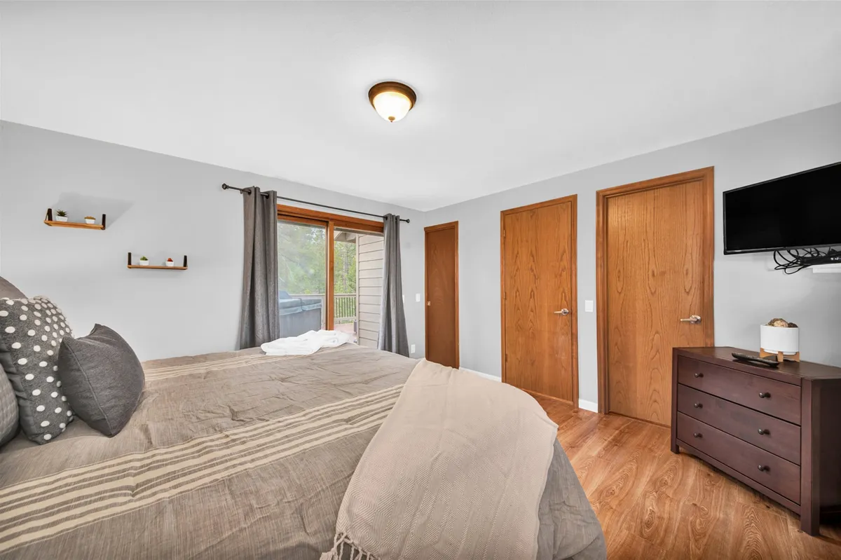A King bedroom with a large window letting in natural light, a comfortable bed with decorative pillows, a dark wood dresser, and a wall-mounted flatscreen TV—creating a cozy retreat for relaxation or enjoying entertainment in privacy.