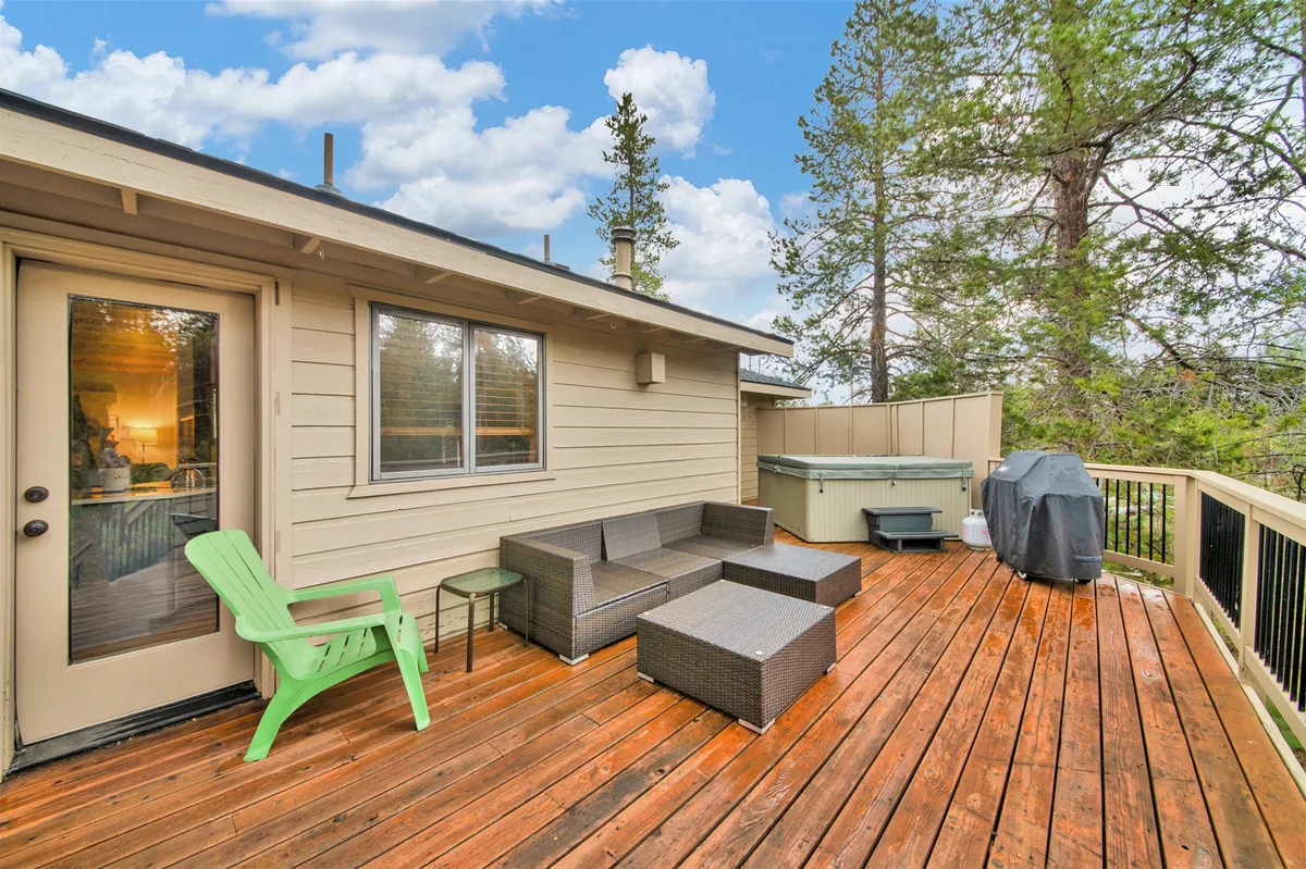 An exterior image of the deck featuring a seating area, hot tub, green chair, and grill, set among natural surroundings. It evokes a relaxed atmosphere for outdoor dining, barbecues, and enjoying nature right off the main living level.