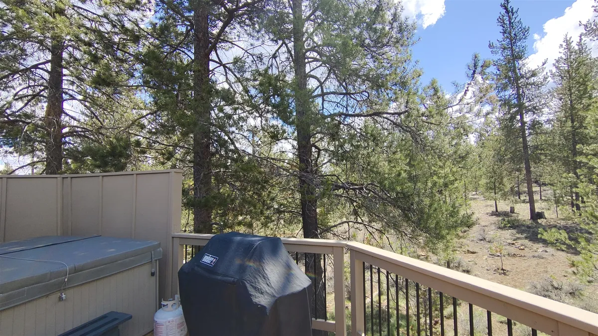 This image captures an inviting outdoor deck surrounded by tall trees, featuring a private hot tub and a grill. The peaceful natural setting highlights opportunities to relax, cook outdoors, and enjoy the tranquility of the surrounding forest.