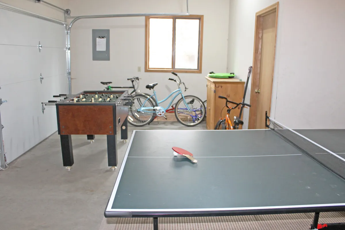 This interior image showcases a spacious garage or game room area, featuring several bicycles, a ping pong table, and a foosball table. The mood is energetic and fun, ideal for active family recreation.