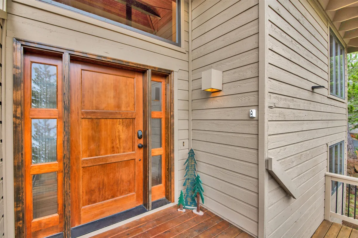 The welcoming entryway of the home, featuring a wooden front door, a decorative green tree, and a modern light fixture. Sunlight streams through the windows, highlighting the connection between the interior and the outdoors and setting the tone for an inviting arrival.