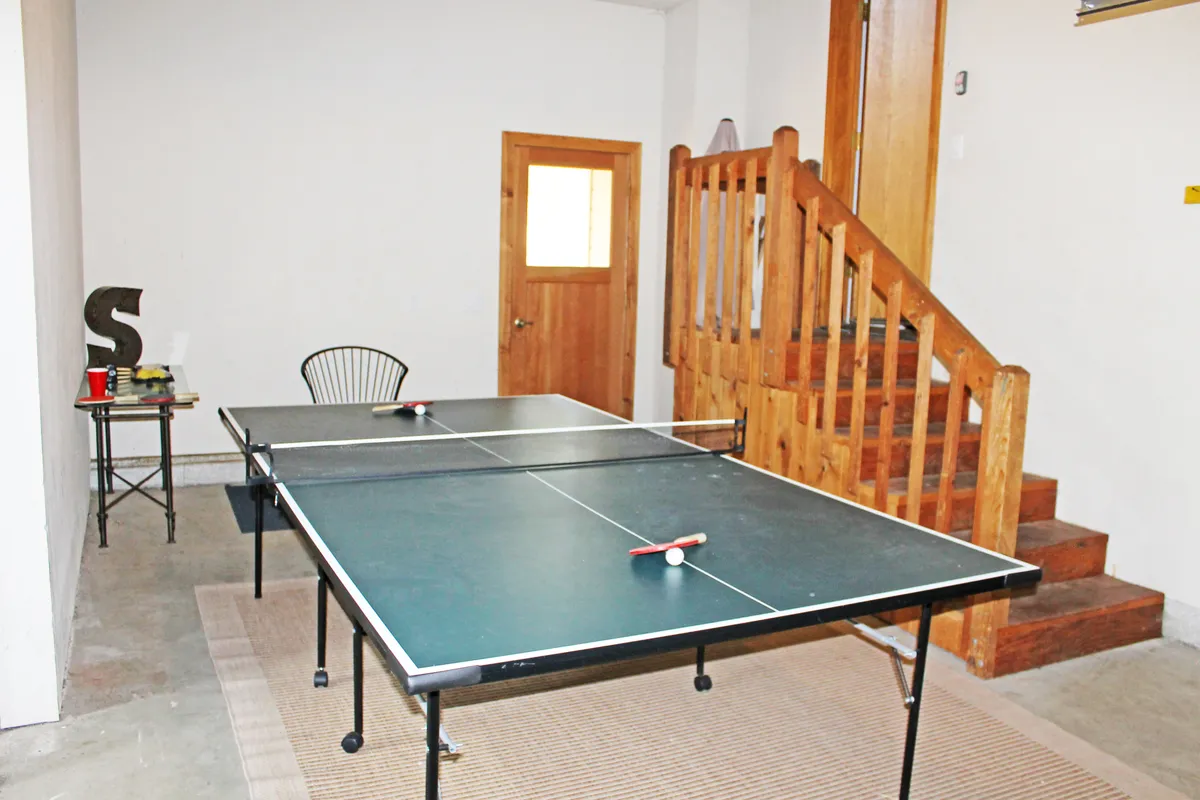 A bright, open space featuring ping pong tables near a staircase and a wooden door, signaling a lively game area. The setting is fun and energetic, suggesting opportunities for friendly family competitions and indoor play.